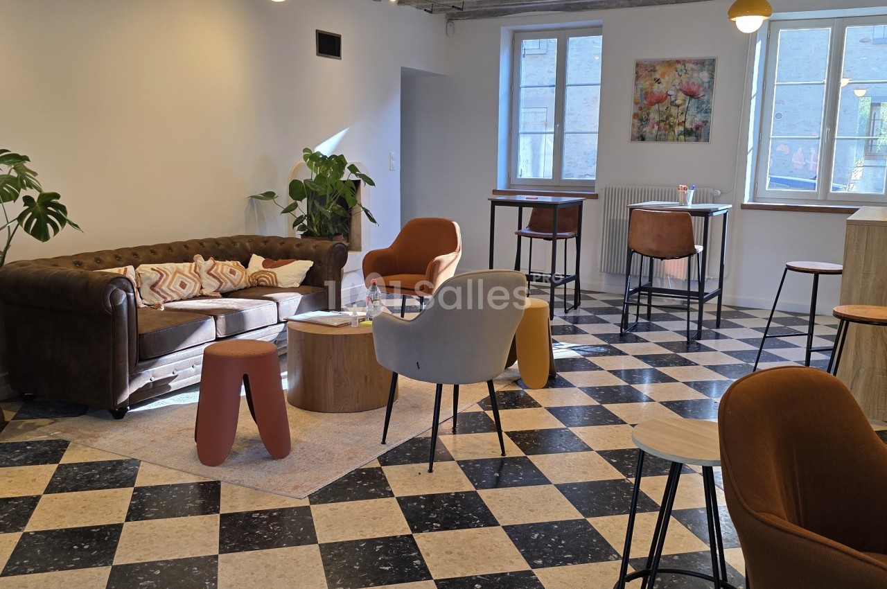Salon aux sols en damier noir et beige, avec un canapé Chesterfield en cuir marron, des fauteuils colorés, des tabourets et des tables hautes près de fenêtres.