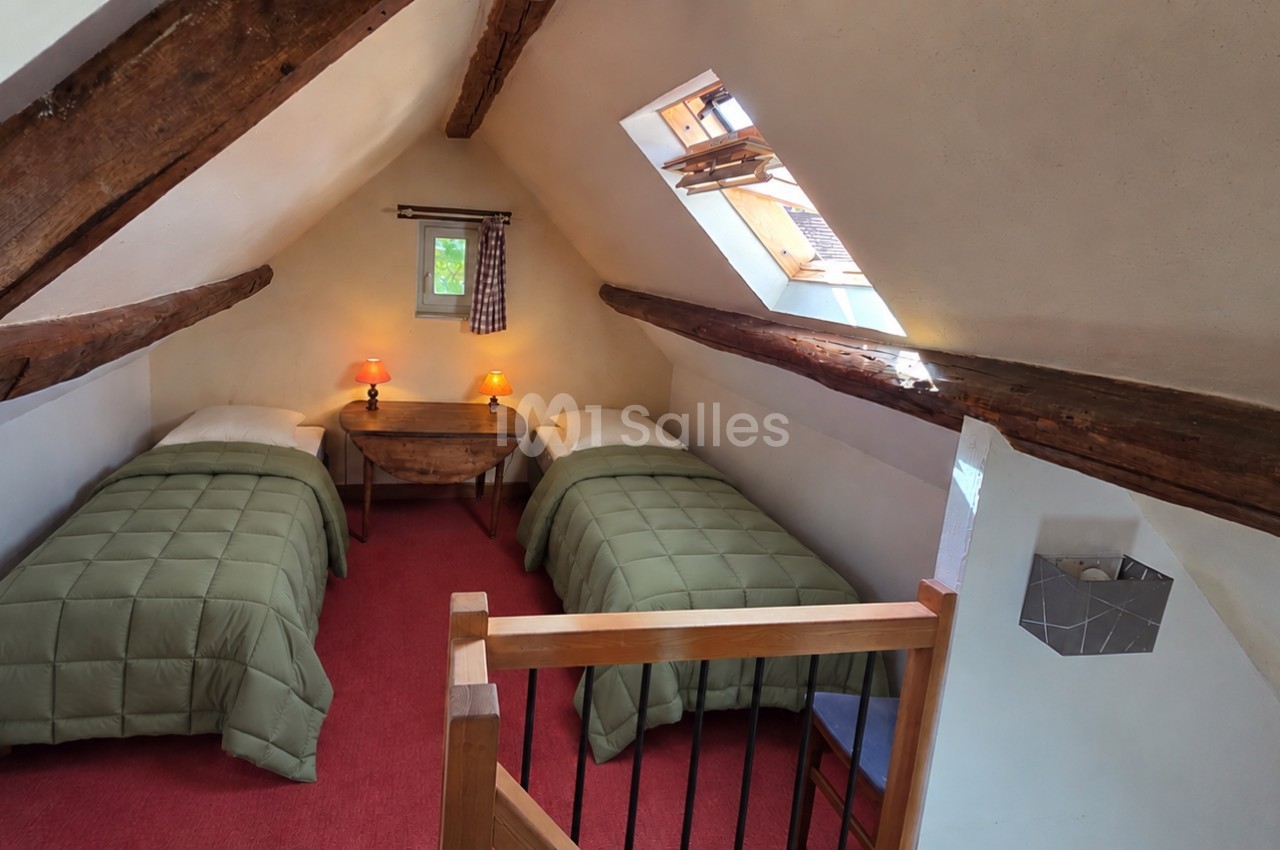 Chambre mansardée aux poutres apparentes avec deux lits simples recouverts de couvettes vertes, moquette rouge et velux. Let me check: the sentence should be under 125 characters. Count roughly: "Chambre mansardée aux poutres apparentes avec deux lits
