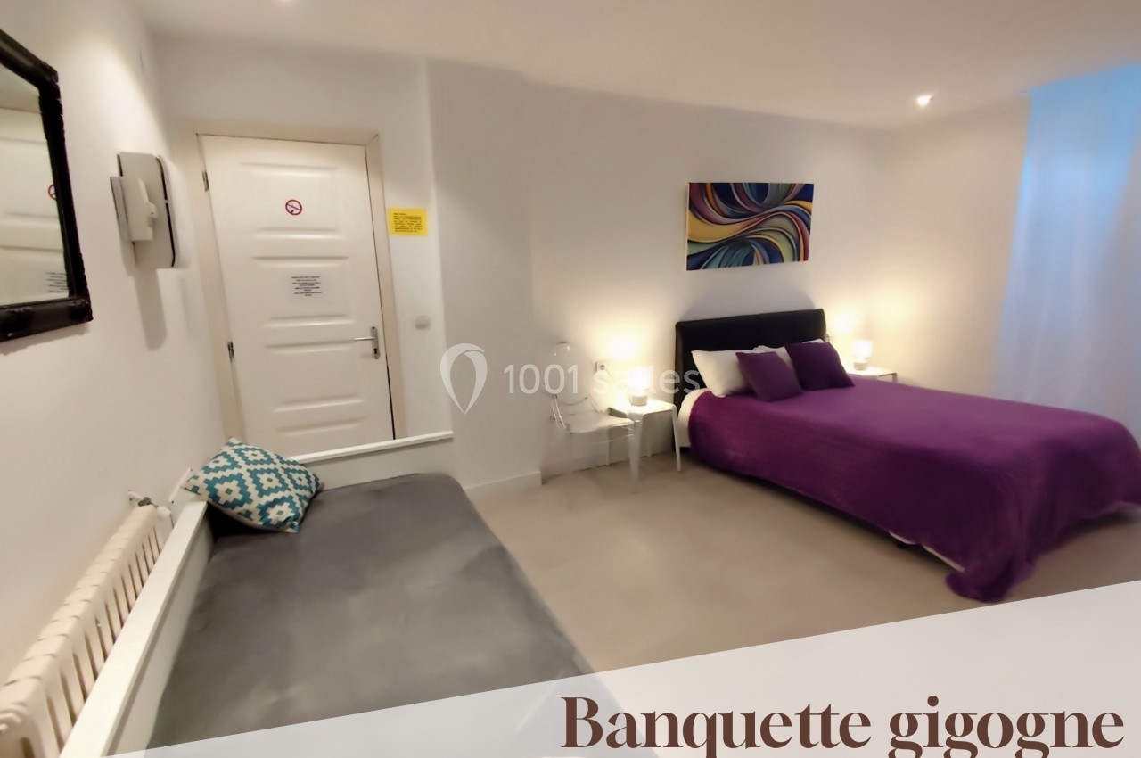 Chambre lumineuse avec un lit double, une banquette gigogne, des murs blancs et une décoration colorée.