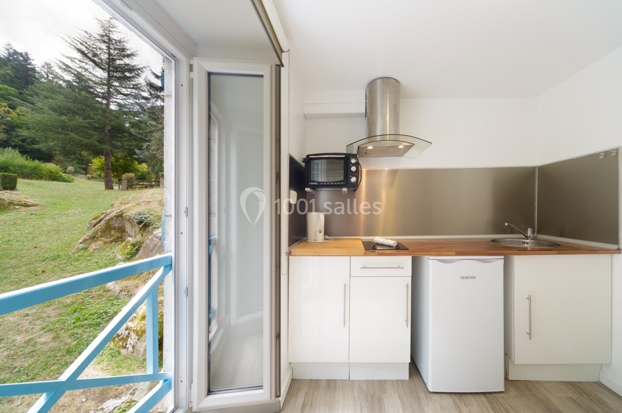 Petite cuisine moderne avec réfrigérateur, micro-ondes, hotte et plan de travail en bois, donnant sur un espace extérieur…