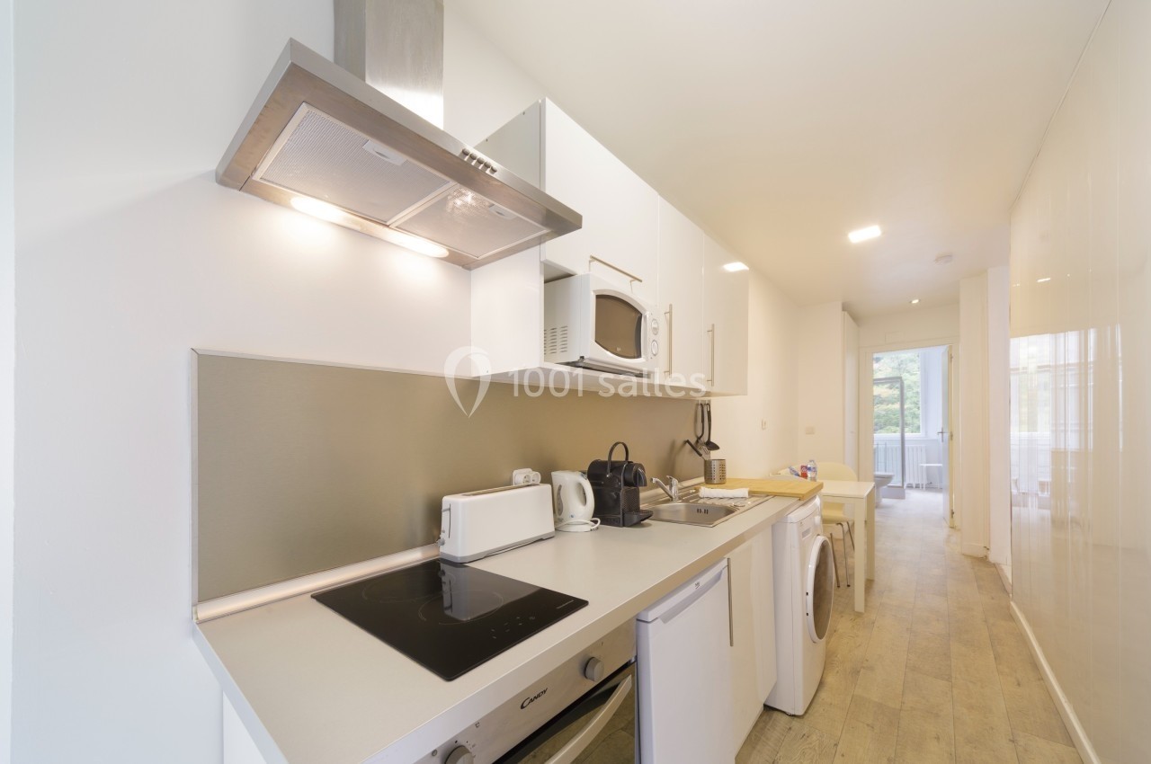 Cuisine moderne avec électroménagers intégrés, plan de travail clair, hotte en inox et vue sur un espace lumineux.