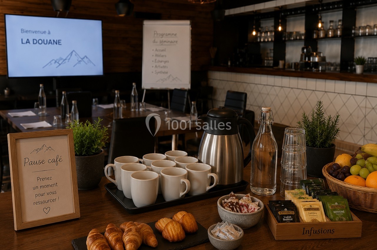 Table avec viennoiseries, boissons chaudes, fruits et infusions, en arrière-plan une salle de réunion aménagée.