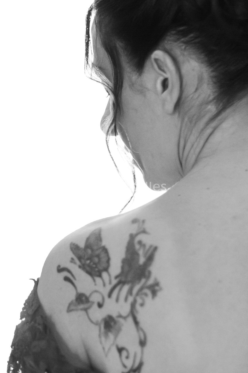 Femme de dos avec un tatouage de papillons et fleurs sur l'épaule, cheveux relevés partiellement.