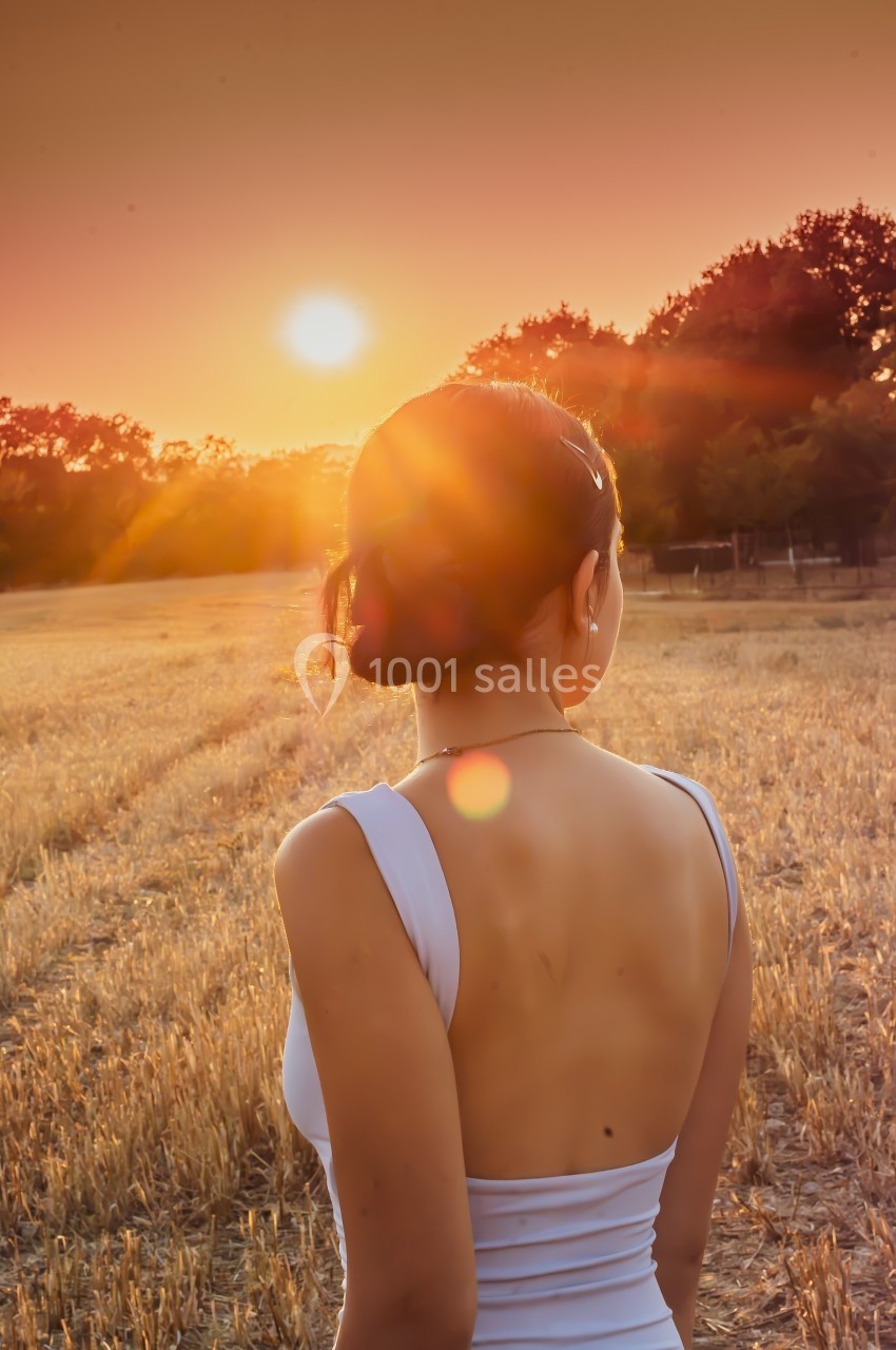 Femme de dos dans un champ au coucher du soleil, portant une robe blanche dos nu.