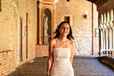 Une femme en robe blanche marche dans une galerie couverte en pierre avec des arches et des murs en briques.