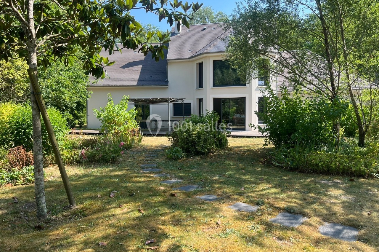 Maison moderne entourée d'un jardin arboré avec pelouse, arbustes et allée en dalles.