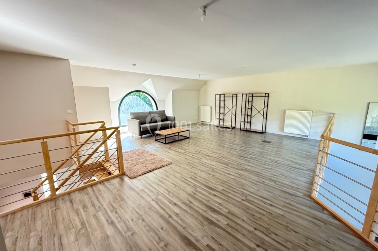 Grande pièce lumineuse avec parquet, canapé, table basse, étagères et escalier en bois, fenêtre en arche visible.