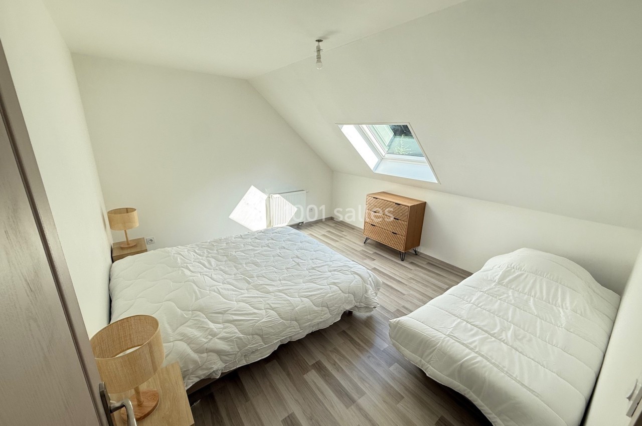 Chambre mansardée avec deux lits simples, parquet clair, une fenêtre de toit et mobilier minimaliste en bois.