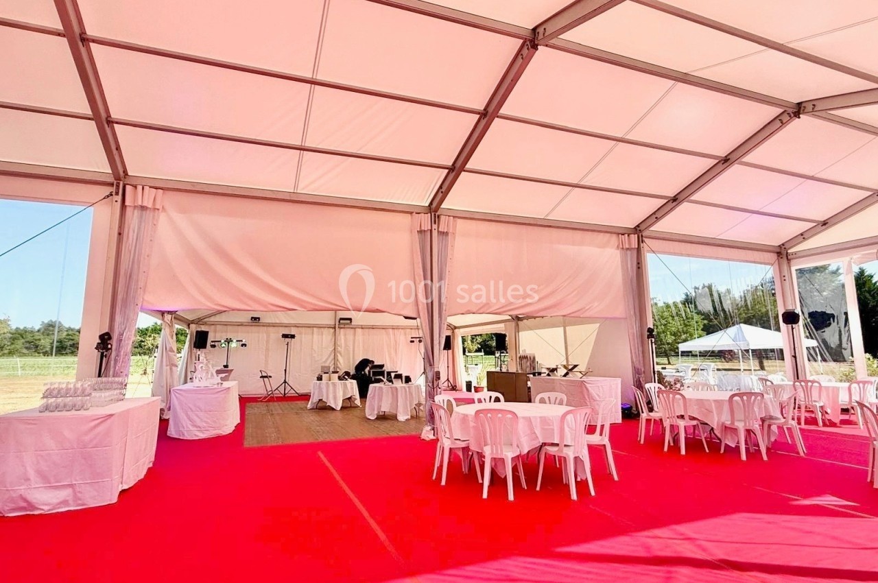 Intérieur d'une tente événementielle avec sol rouge, tables et chaises blanches, équipements audio et buffet en arrière-plan.