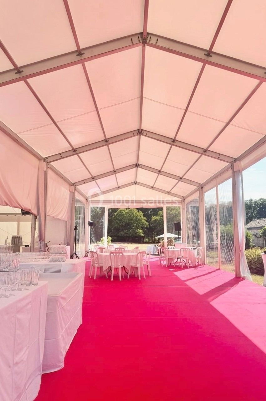 Intérieur d'une tente événementielle avec sol rose, tables blanches et vue sur un espace extérieur verdoyant.