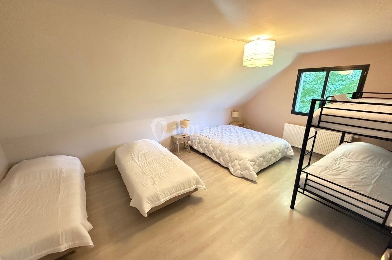 Chambre spacieuse avec trois lits simples, un lit double, un lit superposé et une grande fenêtre donnant sur la verdure.
