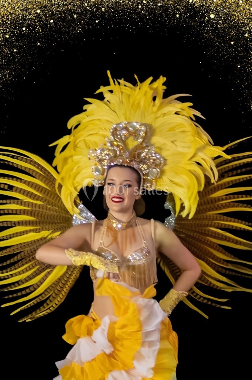 Danseuse en costume jaune à plumes et paillettes, posant devant un fond noir orné de motifs dorés.