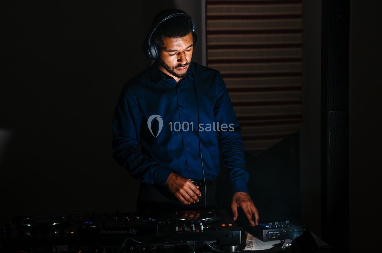 Un DJ mixe de la musique sur une table de mixage dans un environnement faiblement éclairé.