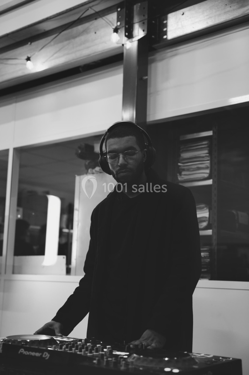 Un DJ concentré mixe de la musique sur une table de mixage dans un espace intérieur moderne.