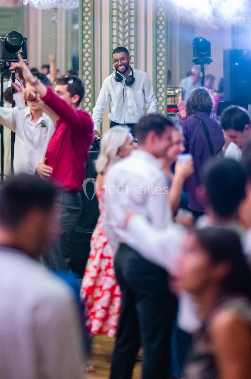 Un DJ souriant anime une piste de danse bondée lors d'une soirée festive dans une salle élégante.