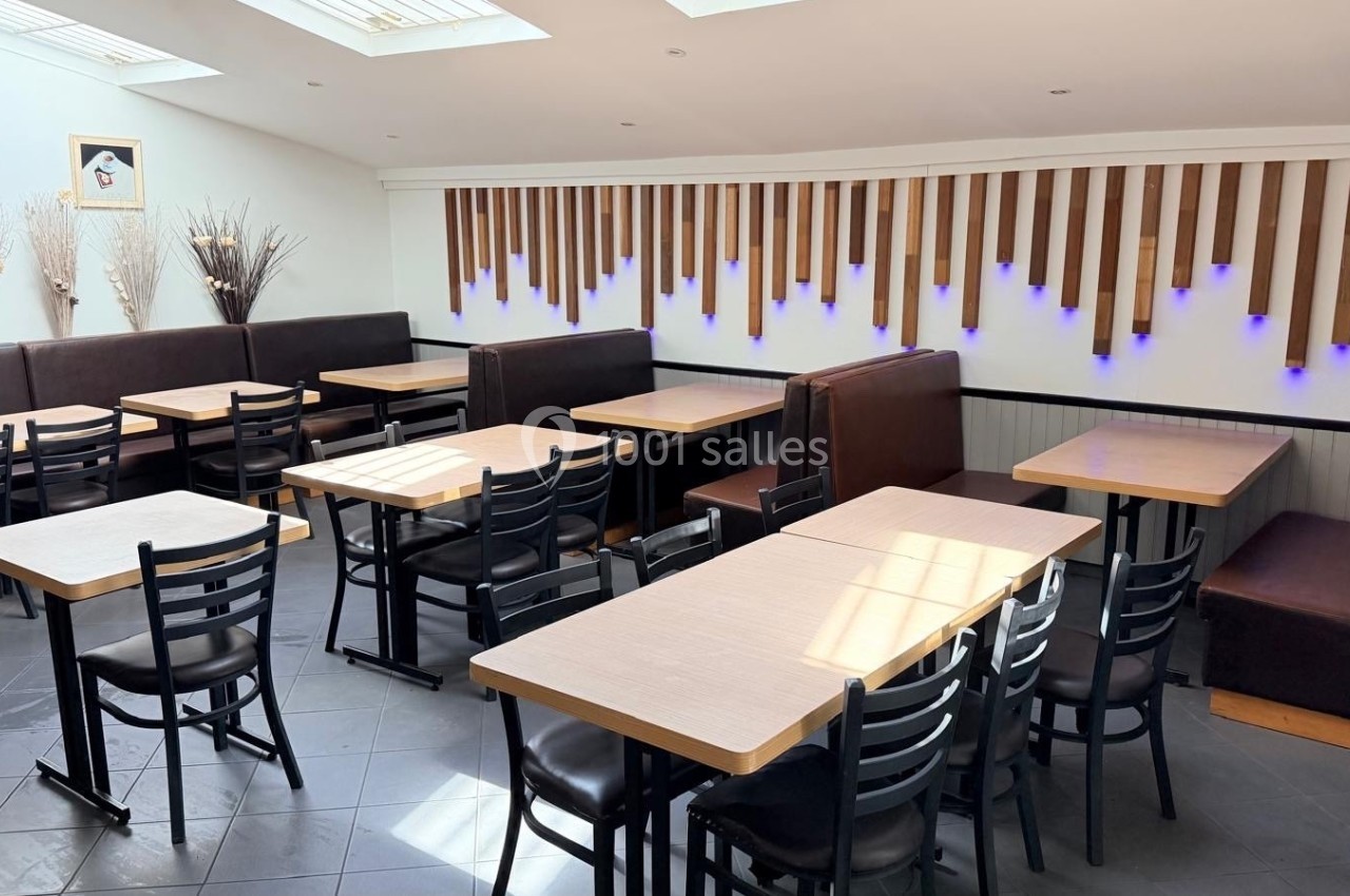 Salle de restaurant lumineuse avec tables en bois clair, chaises noires et banquettes contre un mur décoré de bois et…
