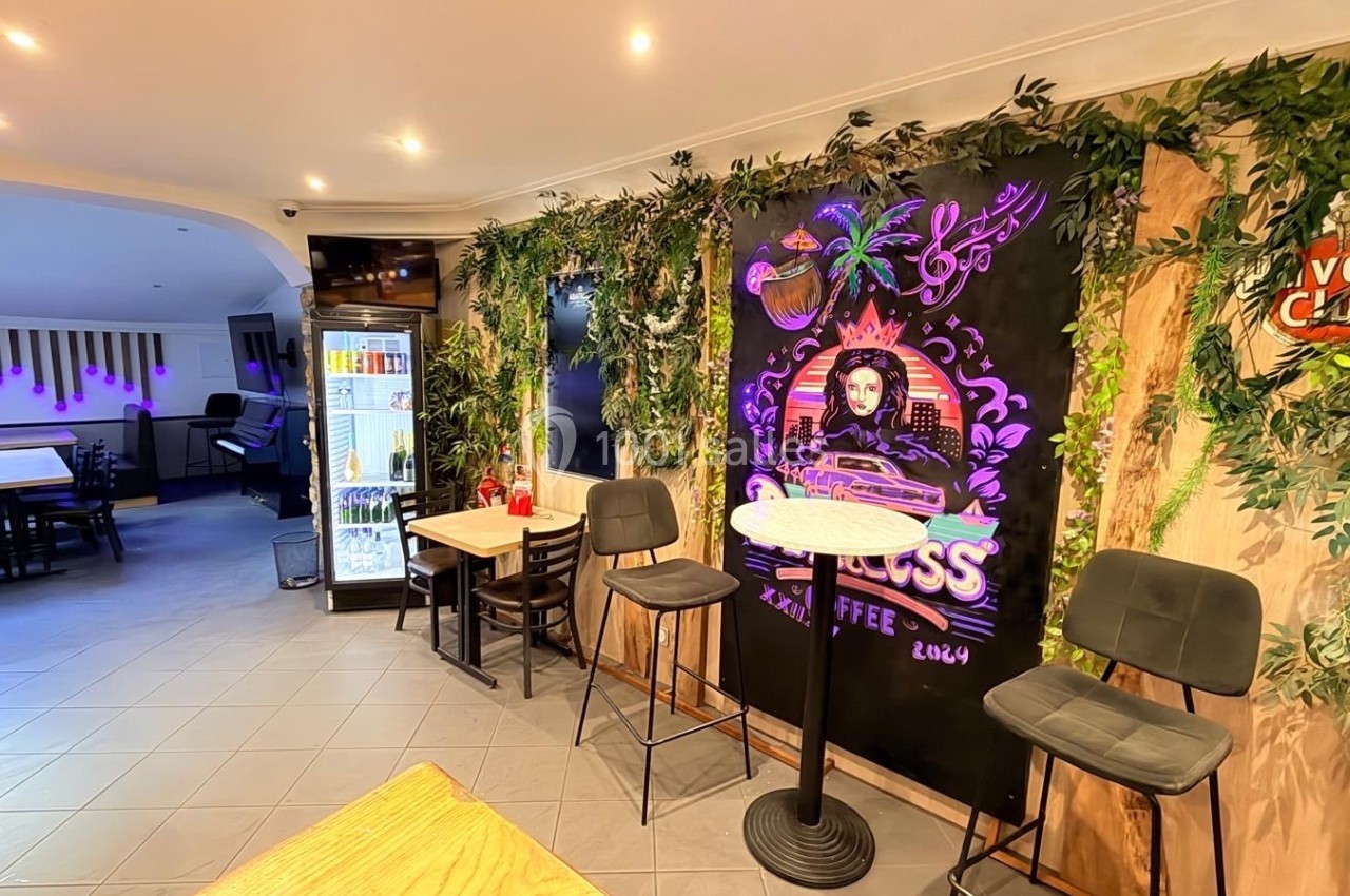 Mur décoré de plantes et d'une fresque colorée dans un café avec tables, chaises et un réfrigérateur en arrière-plan.