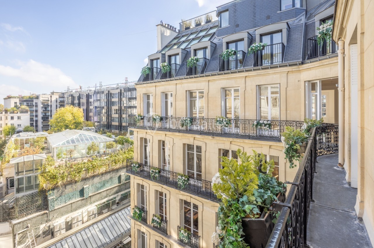 Façade d'un immeuble haussmannien avec balcons fleuris, vue sur une cour intérieure et des bâtiments modernes.