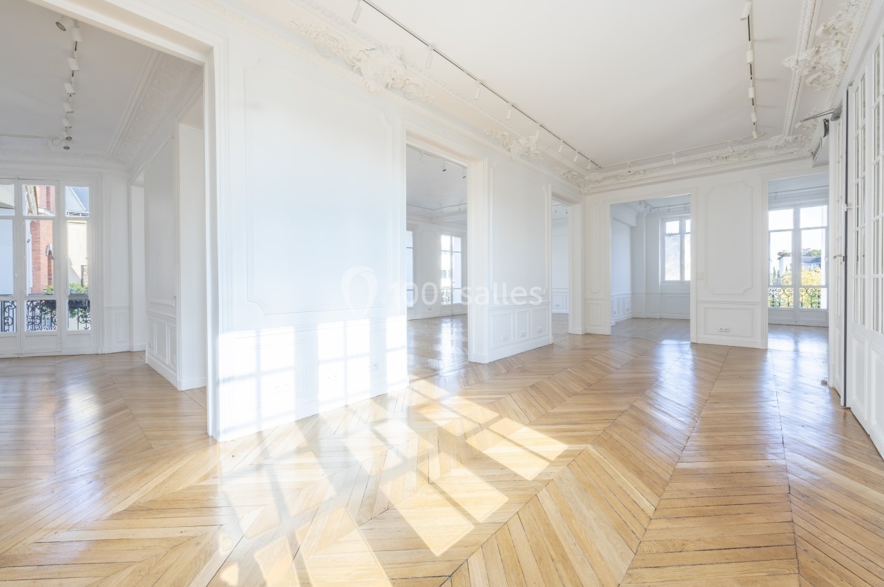 Intérieur lumineux d'un appartement vide avec parquet en bois clair, moulures au plafond et grandes fenêtres.