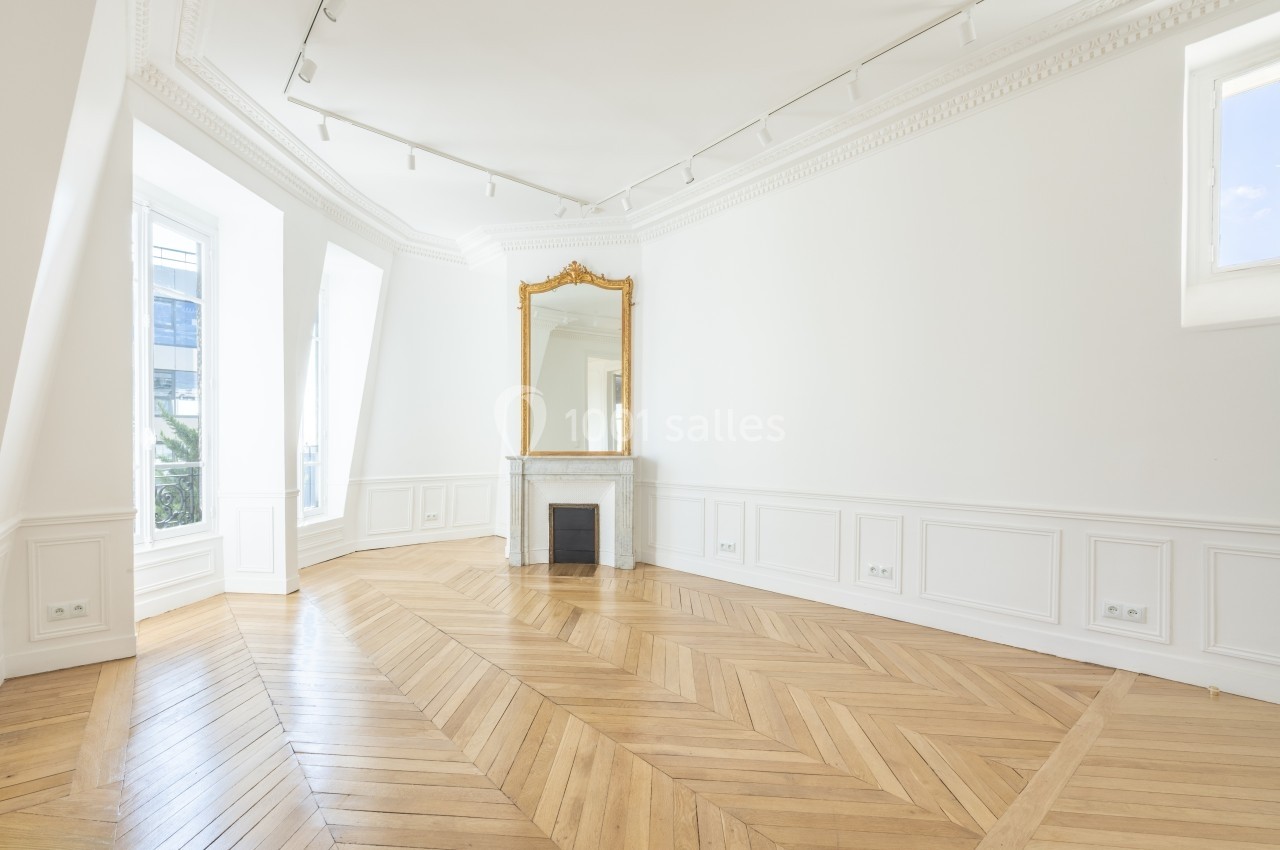Salle lumineuse avec parquet en chevrons, cheminée en marbre, grand miroir doré et moulures blanches.