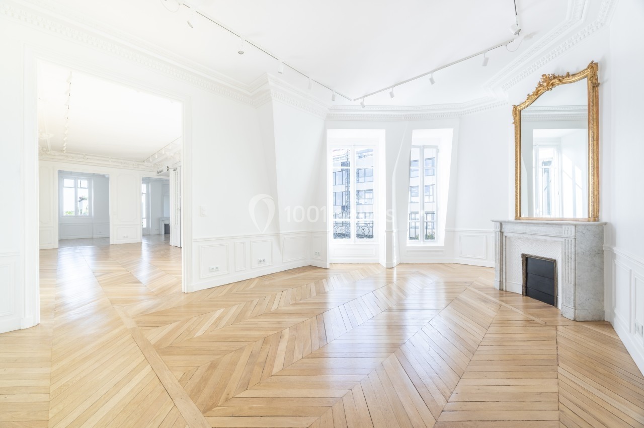 Intérieur lumineux d'un appartement avec parquet en chevrons, cheminée en marbre et grandes fenêtres.
