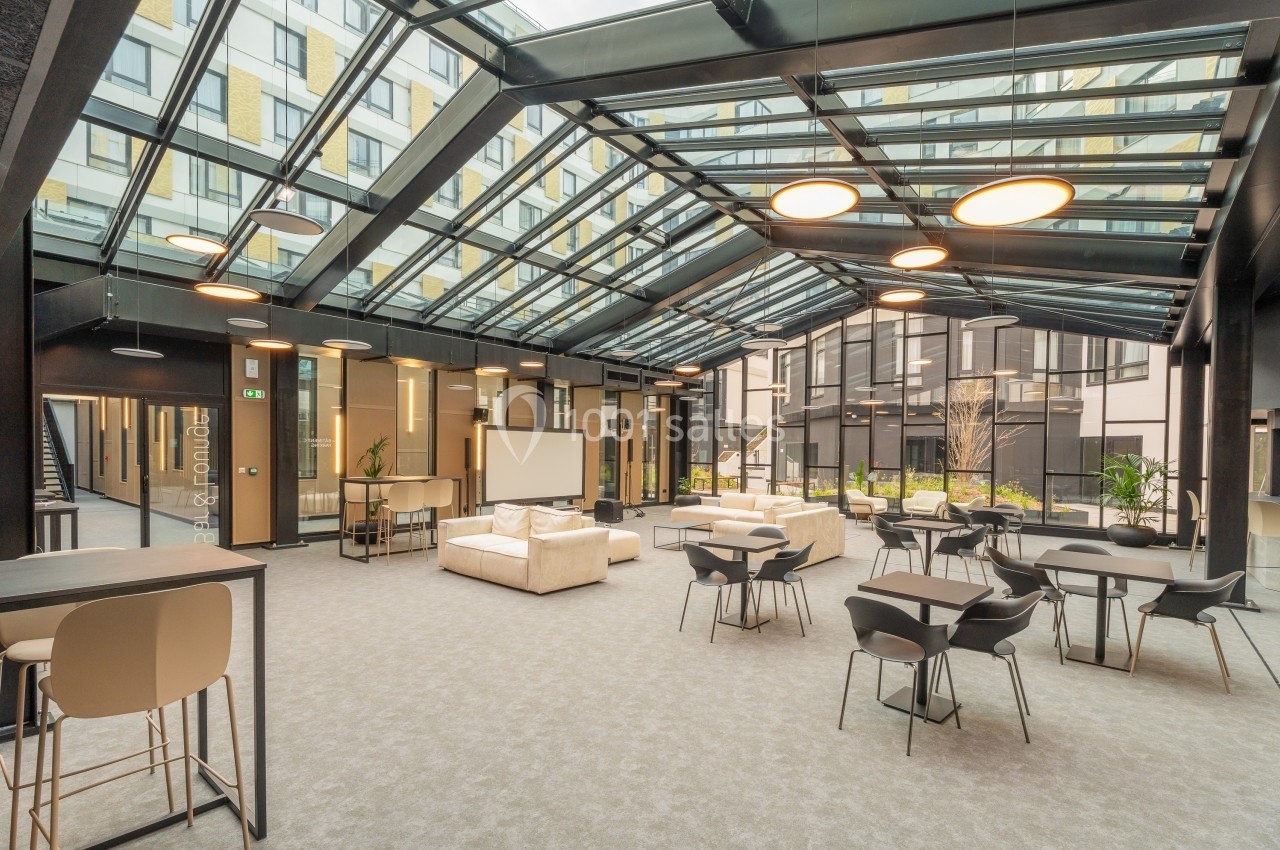 Espace intérieur lumineux avec verrière, mobilier moderne, tables, chaises et canapés, donnant sur une cour.