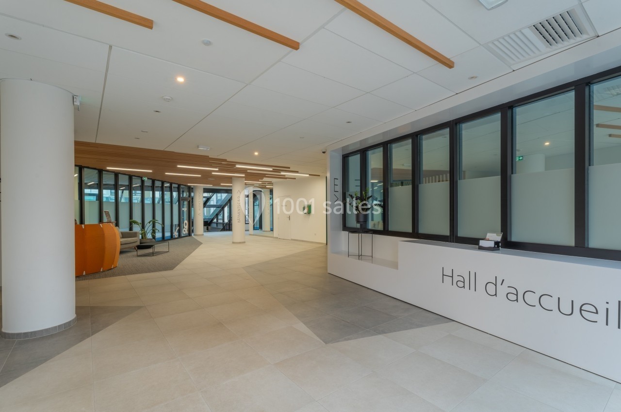 Hall d'accueil moderne avec comptoir, baies vitrées et espace d'attente aménagé dans un bâtiment lumineux.