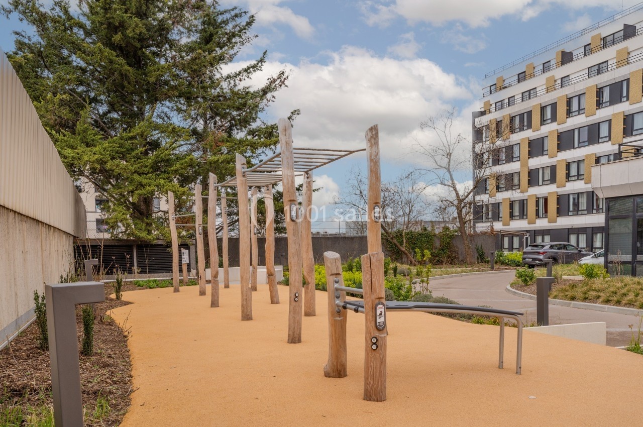 Parcours de fitness extérieur avec agrès en bois, situé dans un espace urbain entouré de bâtiments modernes.