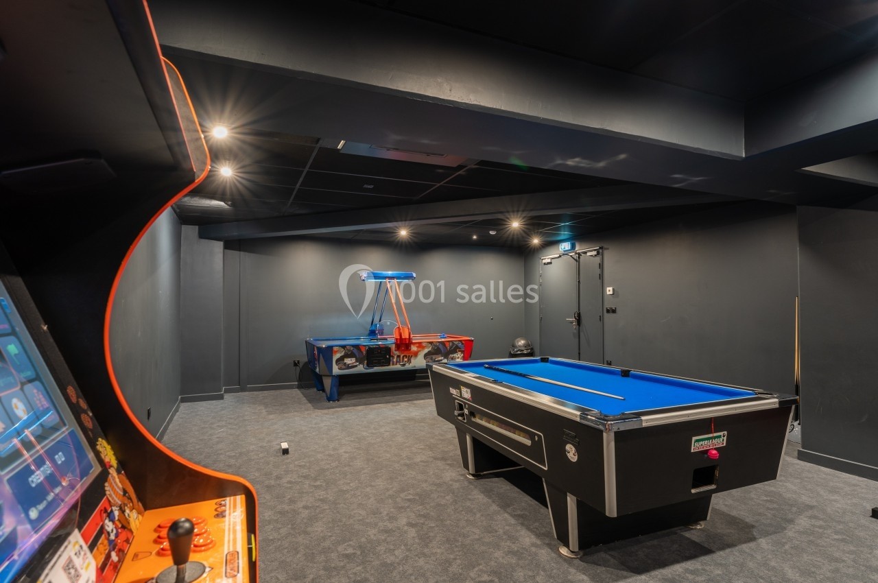 Salle de jeux avec un billard, un air hockey et une borne d'arcade dans un espace sombre au design moderne.