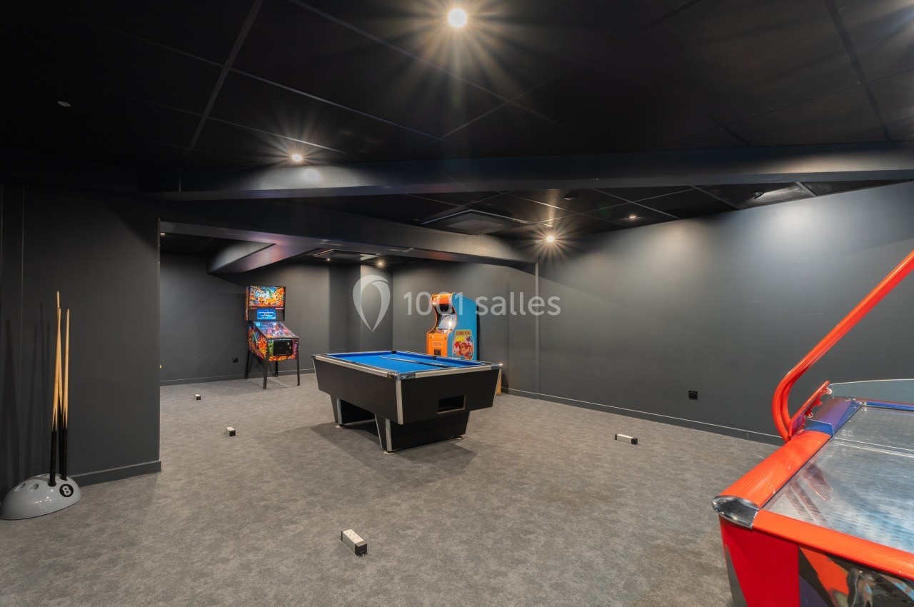 Salle de jeux avec un billard, un baby-foot, des bornes d'arcade et des murs sombres.