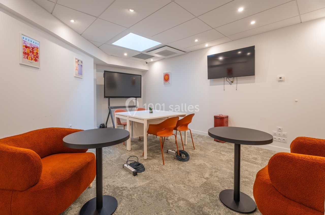 Salle de réunion lumineuse avec table blanche, chaises orange, fauteuils, écran mural et tableau interactif.