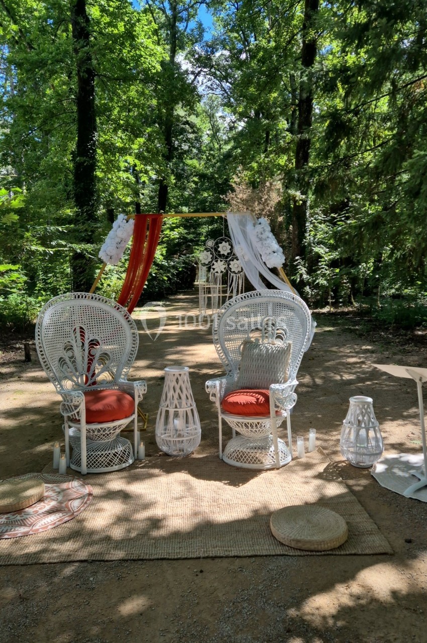 Deux fauteuils en rotin blanc avec coussins rouges, disposés devant une arche décorée dans un cadre boisé.