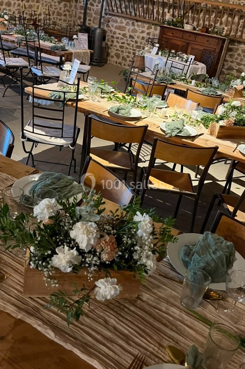 Salle de réception décorée avec des tables en bois, nappes claires, bouquets de fleurs et serviettes vertes.
