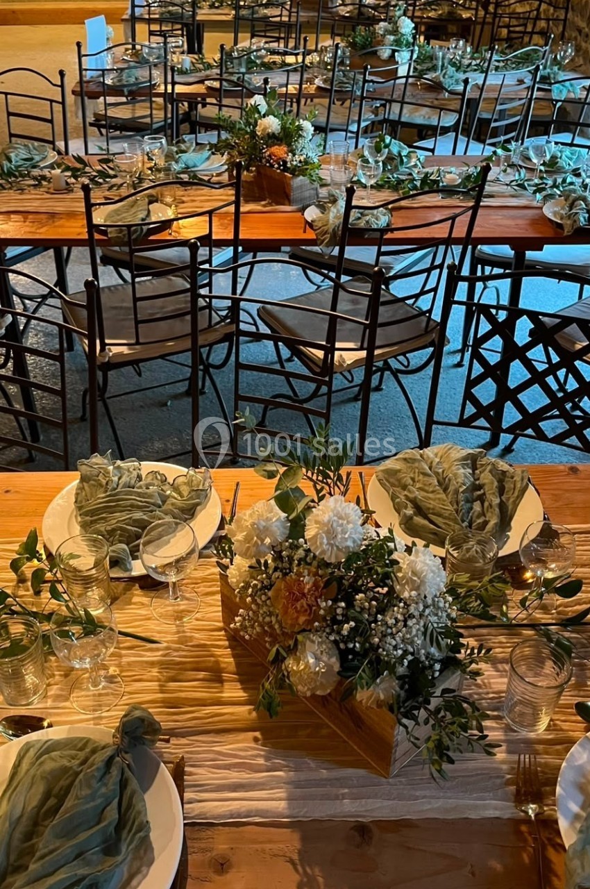 Tables en bois décorées de fleurs, vaisselle et serviettes en tissu vert, disposées pour un repas festif en intérieur.