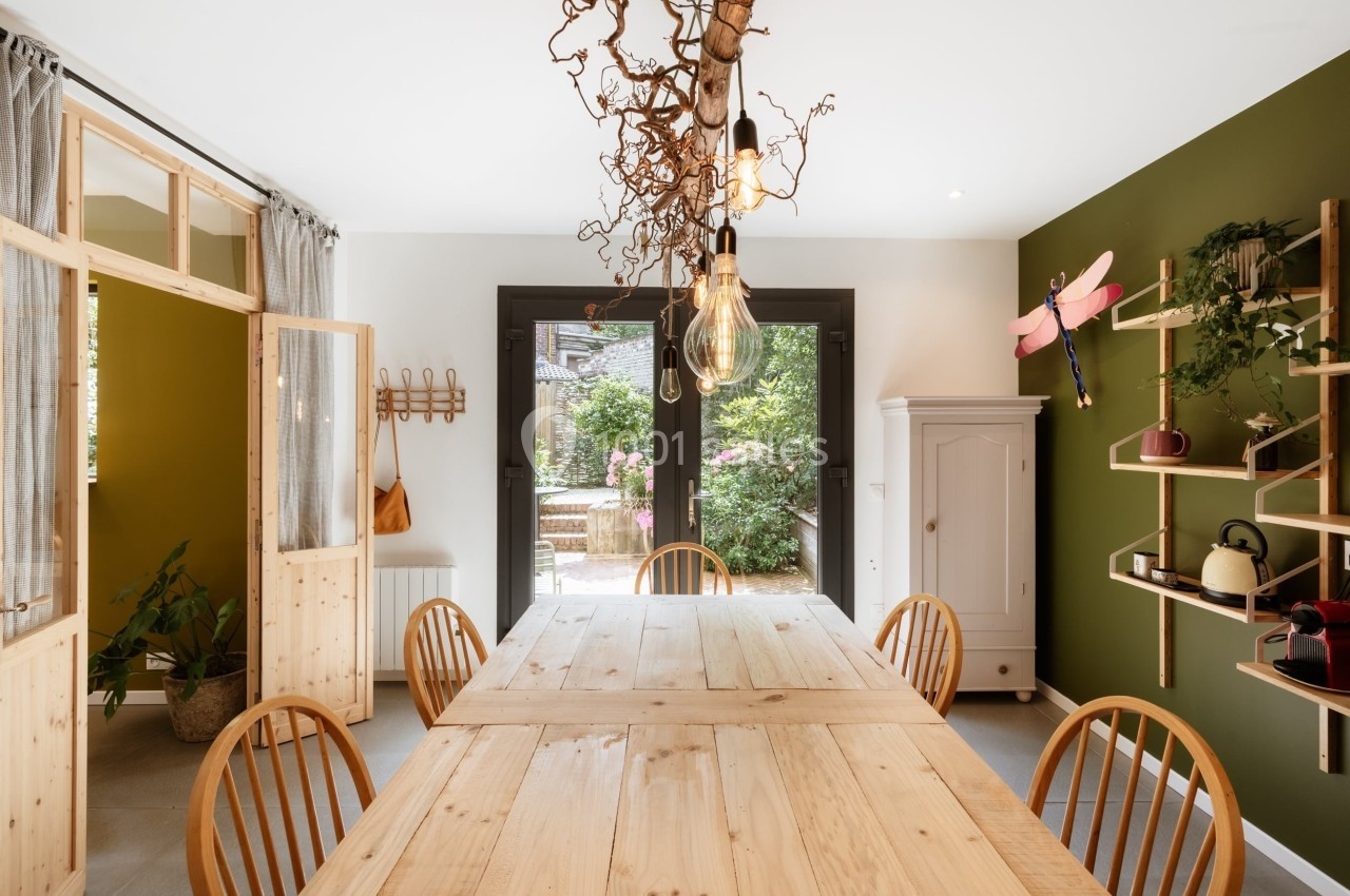 Salle à manger lumineuse avec table en bois, chaises assorties, étagères murales et vue sur un jardin verdoyant.
