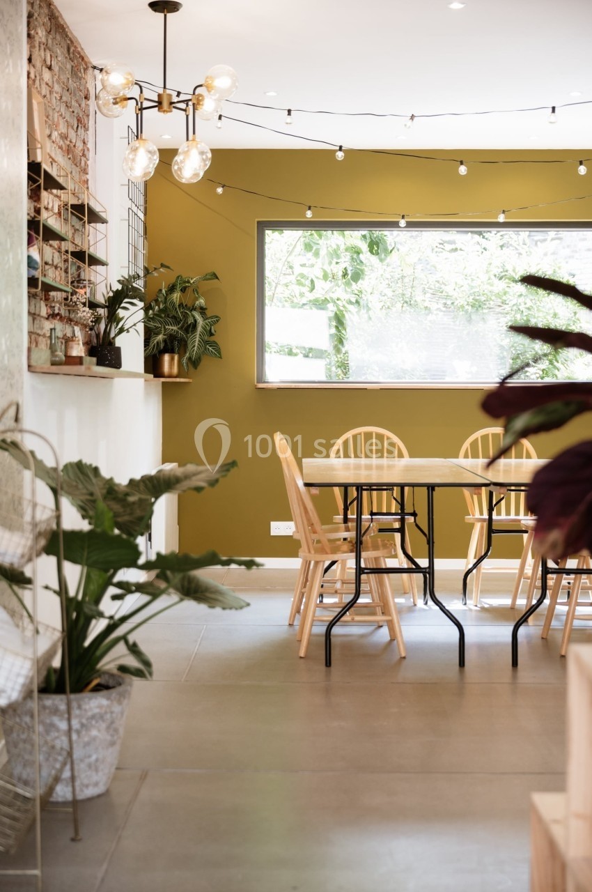 Salle à manger lumineuse avec table en bois, chaises assorties, plantes décoratives et mur vert olive.