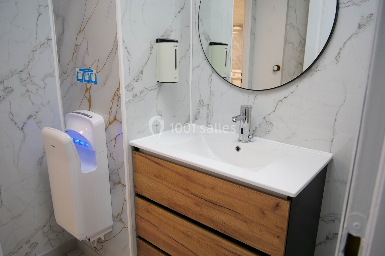 Lavabo avec meuble en bois, miroir rond, mur en marbre et sèche-mains mural dans une salle de bain moderne.