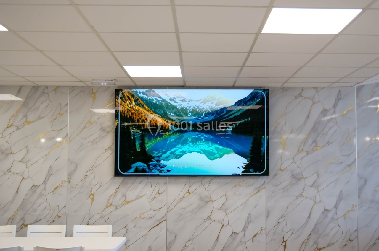 Écran mural affichant un paysage de montagne avec un lac reflétant les sommets, dans une salle aux murs en marbre.