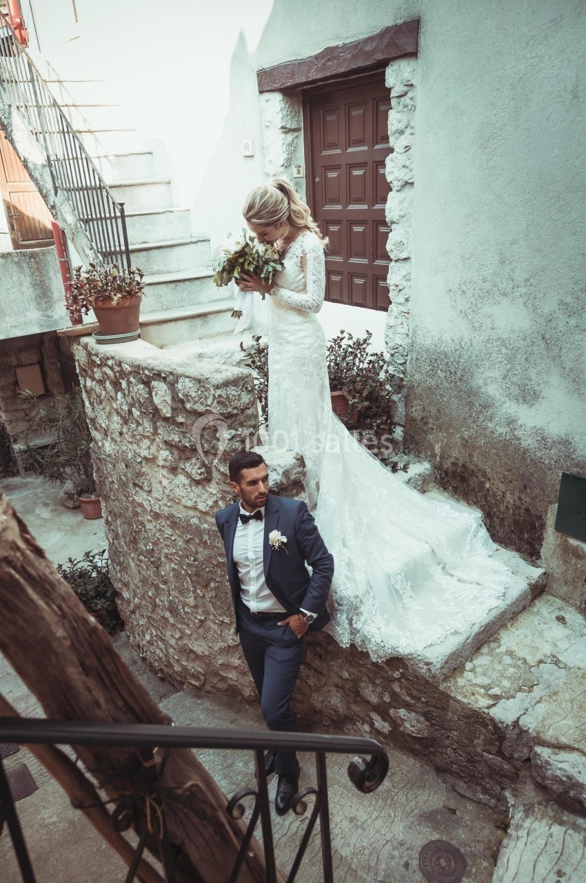 Un couple de mariés pose dans une ruelle en pierre, la mariée tenant un bouquet et descendant un escalier.