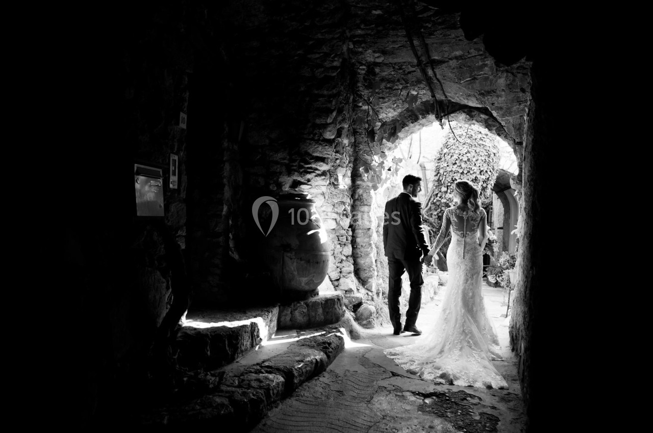 Un couple en tenue de mariage marche main dans la main dans une ruine en pierre éclairée par la lumière naturelle.