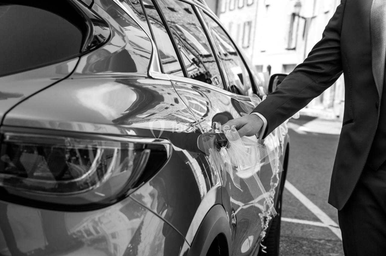 Un homme en costume ouvre la portière d'une voiture stationnée dans une rue urbaine.