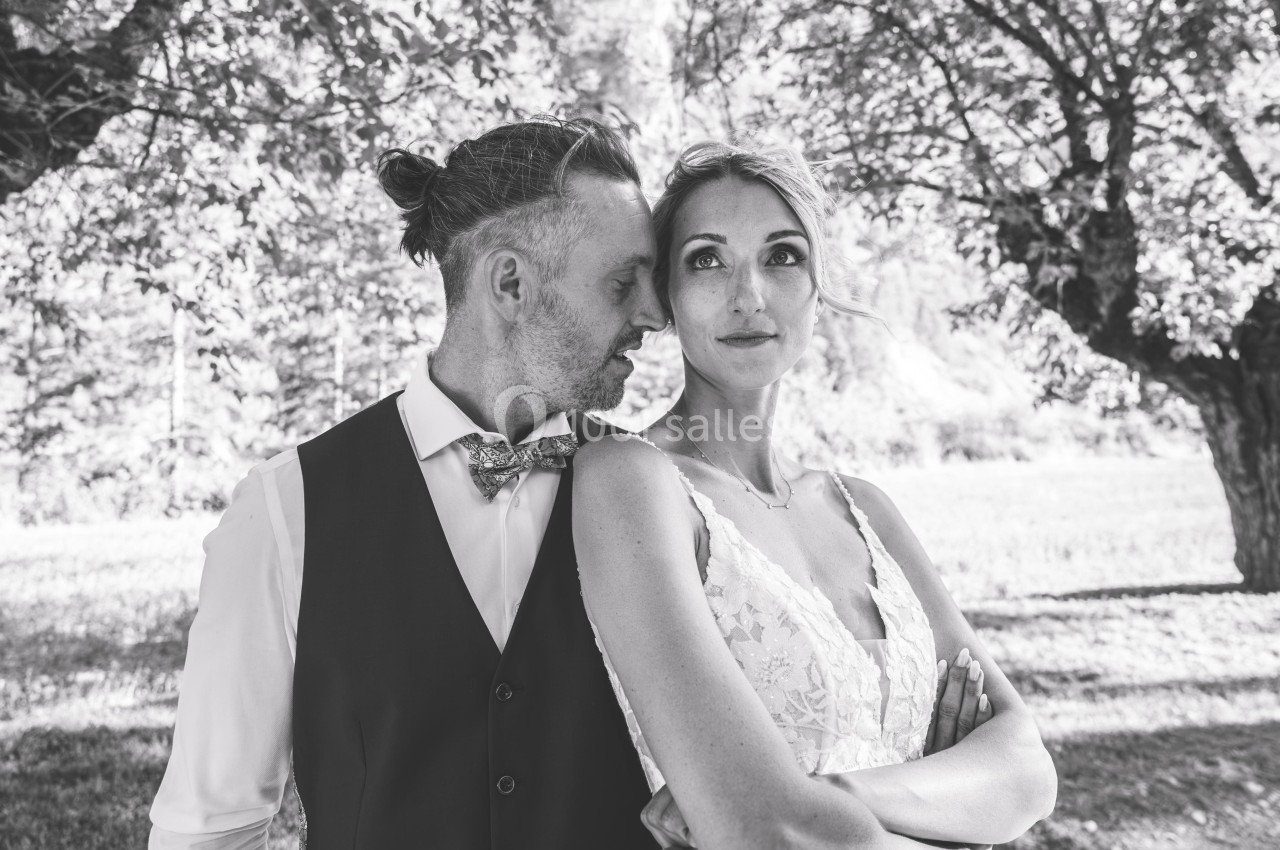 Un couple pose dans un parc, l'homme chuchote près de l'oreille de la femme qui regarde devant elle.