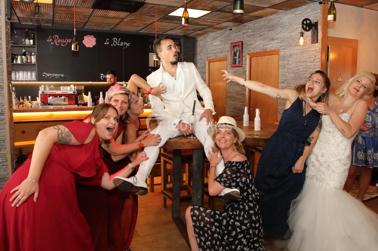 Un homme en costume blanc assis sur une table entouré de femmes souriantes dans un bar décoré.