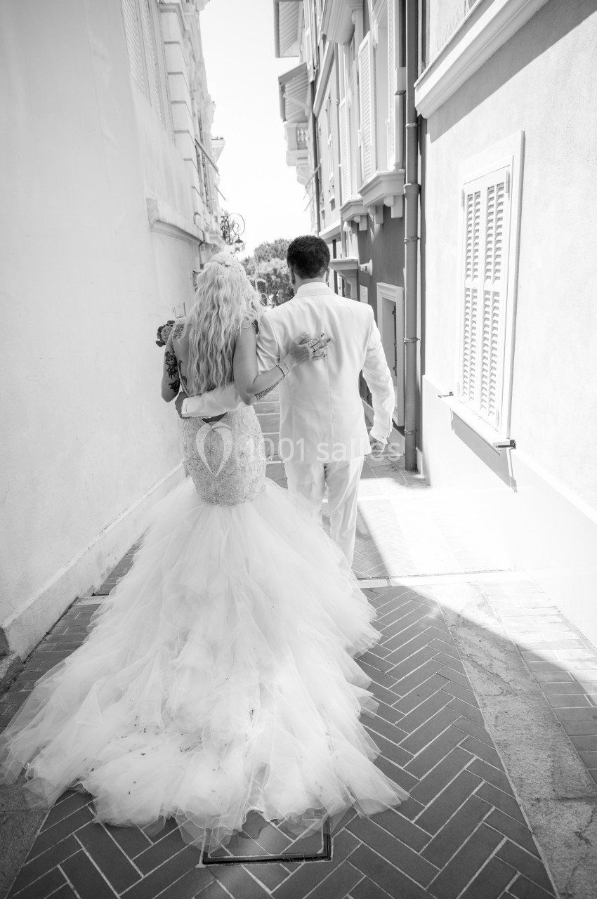 Un couple en tenue de mariage marche dans une ruelle pavée, vu de dos, sous une lumière naturelle.
