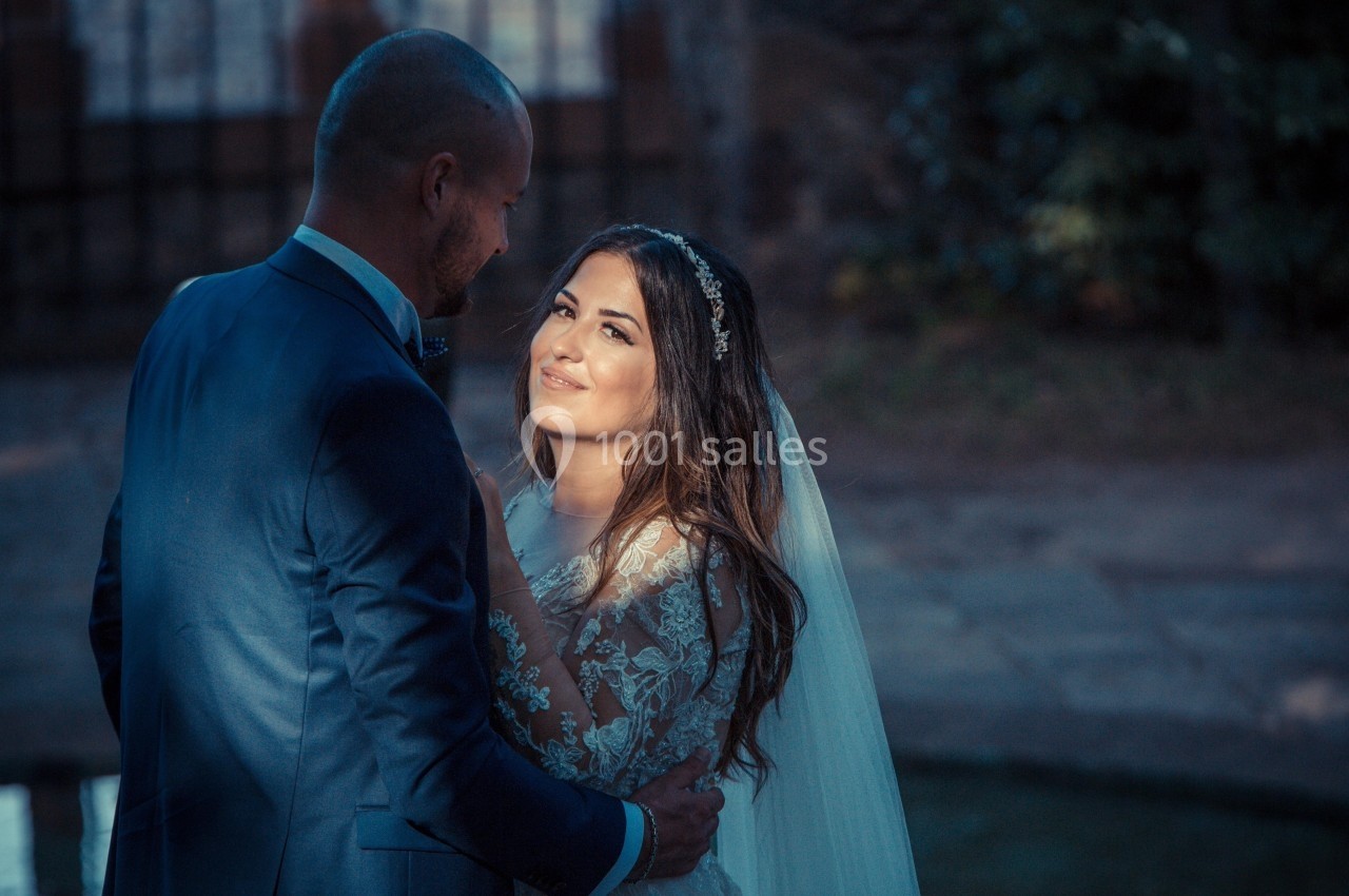 Un couple en tenue de mariage se regarde avec tendresse dans un jardin à la lumière du soir.