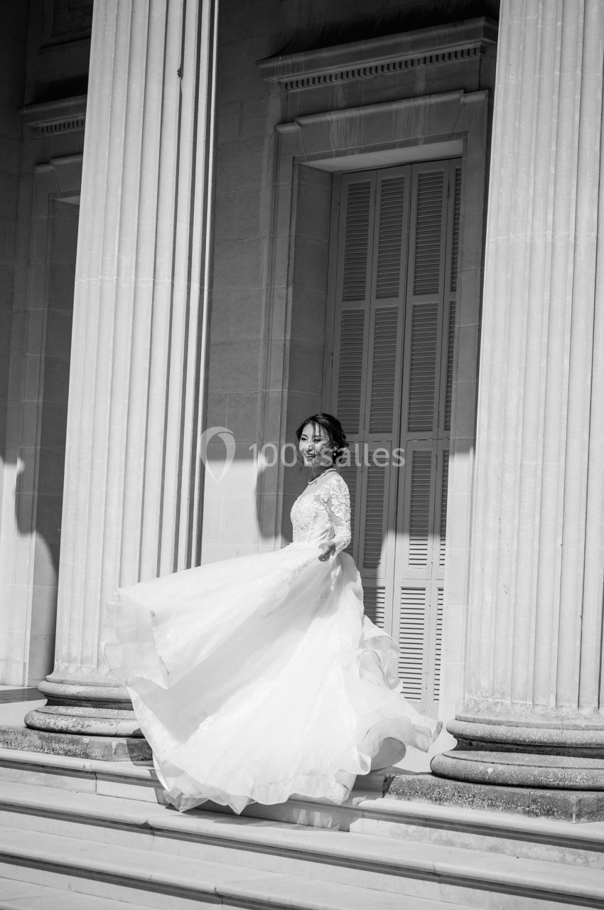 Femme en robe de mariée tournant sur des marches devant un bâtiment à colonnes.