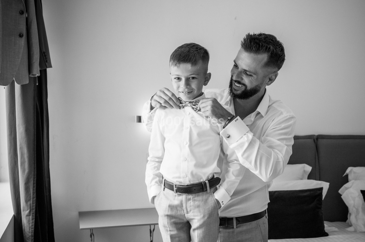 Un homme ajuste le nœud papillon d'un enfant habillé élégamment dans une chambre lumineuse.