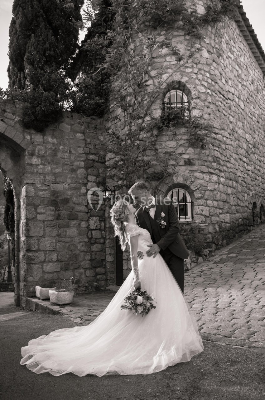 Un couple de mariés pose devant un bâtiment en pierre, la mariée tenant un bouquet de fleurs.