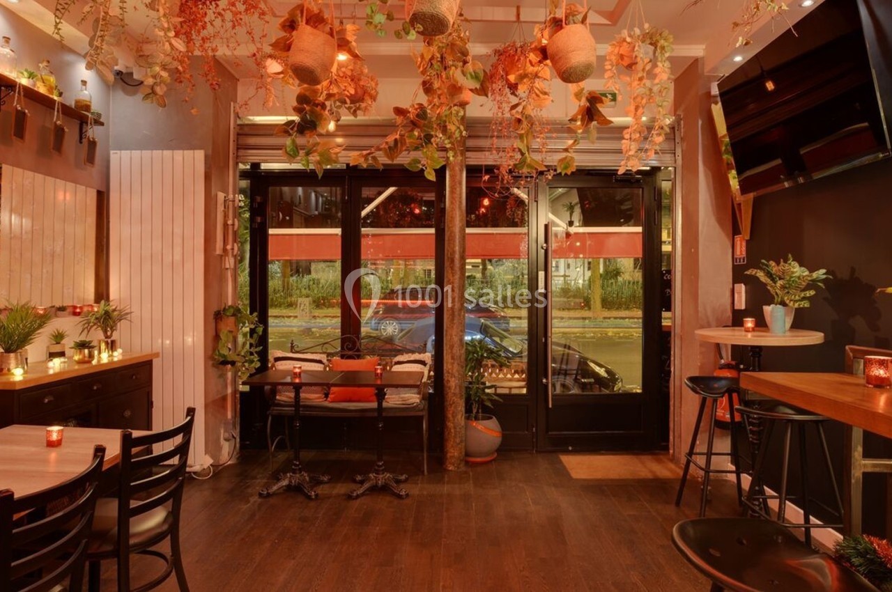 Salle de restaurant chaleureuse avec décoration végétale suspendue, éclairage tamisé et grandes baies vitrées donnant sur la…