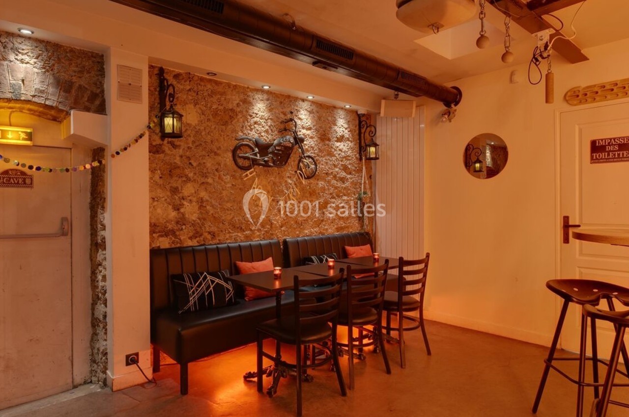 Salle chaleureuse avec murs en pierre, banquette, table et chaises, éclairage tamisé et décoration murale.